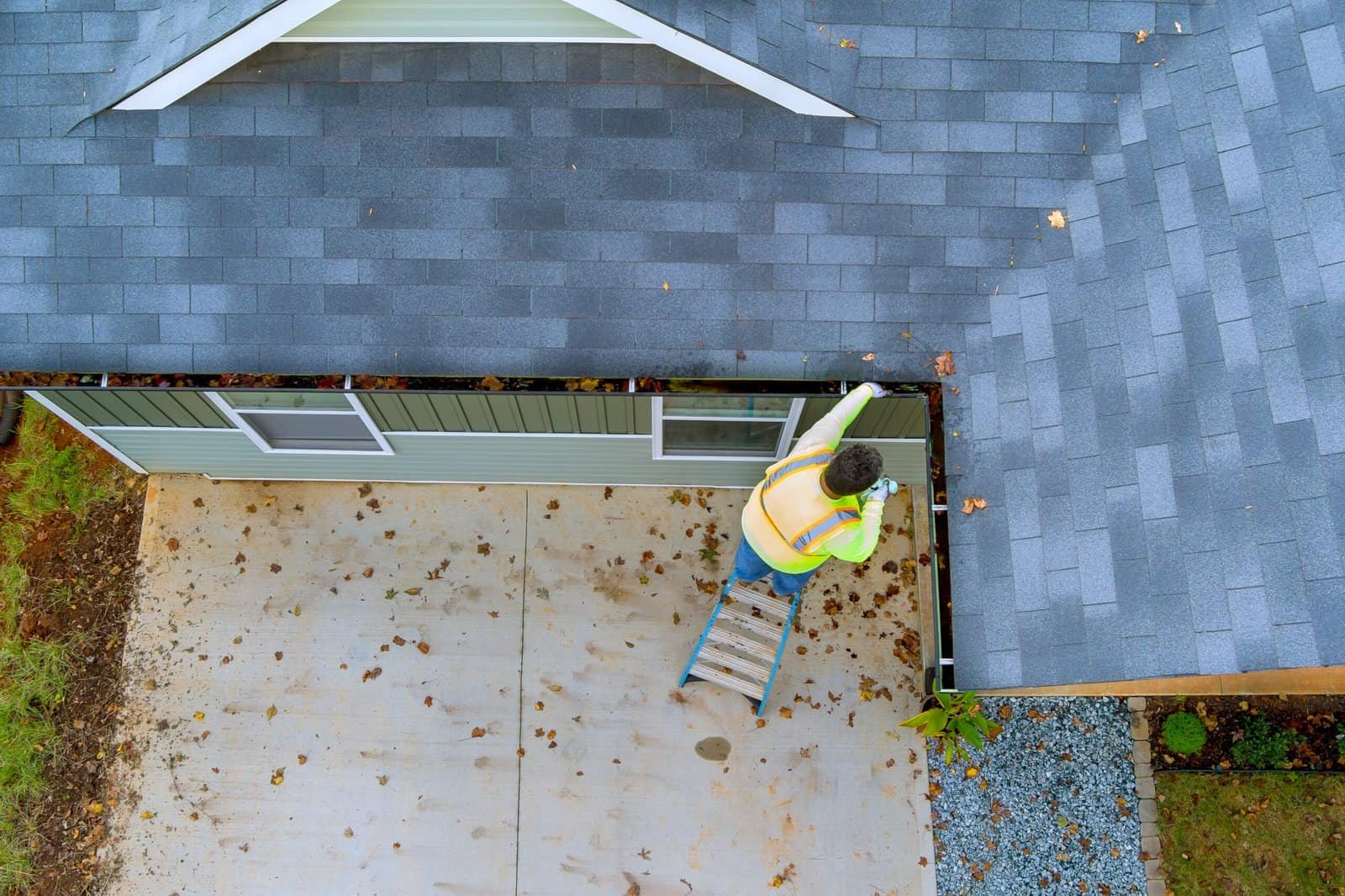 Roofing contractor inspecting roof shingles from ladder in Redlands, CA.